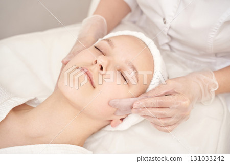Young caucasian female receiving facial treatment in spa setting with gloves 131033242