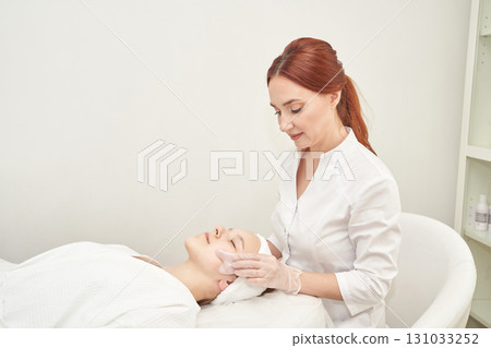 Female esthetician performing facial treatment on young caucasian woman in spa 131033252