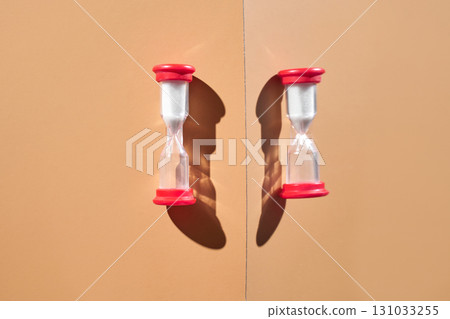 Symmetrical red hourglasses on beige background with shadows reflecting time 131033255