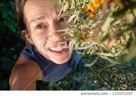 Happy woman looking up at sea buckthorn berries, harvesting natural and healthy food from bush. Happy woman looking up at sea buckthorn berries, harvesting natural and healthy food from bush. 131033287