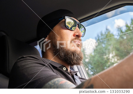 Man with beard and sunglasses driving car on sunny day. 131033290