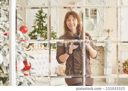 Young caucasian female photographer reflecting in mirror with christmas tree Young caucasian female photographer reflecting in mirror with christmas tree 131033325