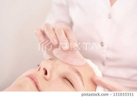 Young caucasian female receiving facial treatment with rose quartz gua sha 131033331