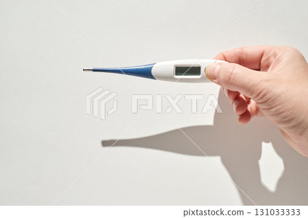 Caucasian adult hand holding digital thermometer against white background Caucasian adult hand holding digital thermometer against white background 131033333