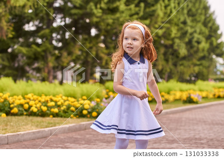 Young caucasian girl in white dress strolling through park with yellow flowers 131033338