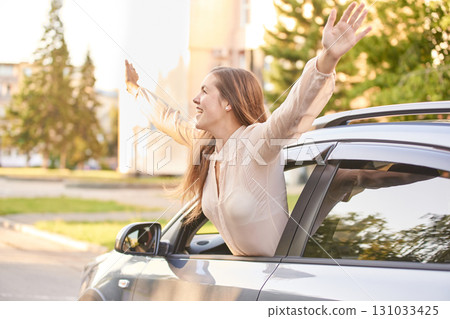 Caucasian young female enjoying freedom leaning out of car window on sunny day Caucasian young female enjoying freedom leaning out of car window on sunny day 131033425