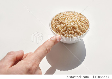 Hand pointing to bowl of uncooked brown rice on white background highlighting Hand pointing to bowl of uncooked brown rice on white background highlighting 131033447