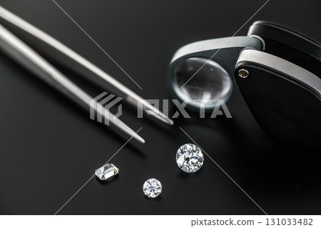 A close up of a diamond ring, a pair of diamond tweezers, and a magnifying glass A close up of a diamond ring, a pair of diamond tweezers, and a magnifying glass 131033482