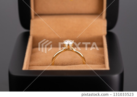 A gold ring with a diamond in the center sits in a black box 131033523