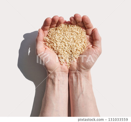 Caucasian hands holding raw brown rice grains against light background 131033559