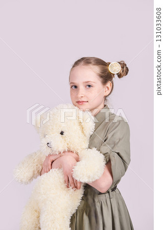 Young caucasian female child holding fluffy teddy bear in gray dress against Young caucasian female child holding fluffy teddy bear in gray dress against 131033608