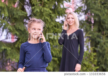 Caucasian child and adult female using smartphones in outdoor park setting Caucasian child and adult female using smartphones in outdoor park setting 131033656