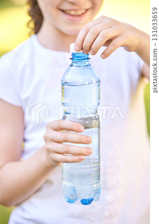 Caucasian child holding plastic water bottle outdoors with smile and white 131033659