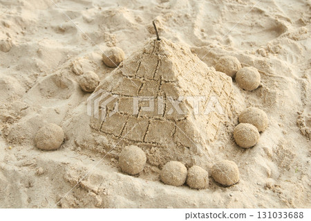 Sand pyramid on beach surrounded by spherical sand sculptures in sunlit setting 131033688