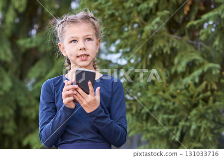 Caucasian young girl using smartphone outdoors in front of pine trees Caucasian young girl using smartphone outdoors in front of pine trees 131033716