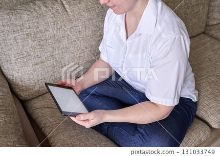 Caucasian adult female reading on digital tablet while sitting on comfortable Caucasian adult female reading on digital tablet while sitting on comfortable 131033749
