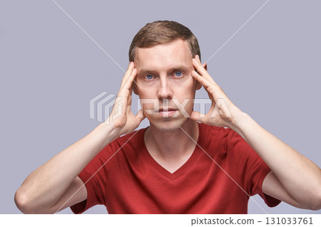 Caucasian male adult holding head in red shirt on gray background 131033761