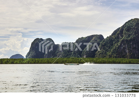 Longtail boat cruising near limestone cliffs in serene tropical landscape 131033778