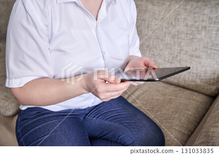 Caucasian woman using tablet in casual setting wearing white shirt and jeans Caucasian woman using tablet in casual setting wearing white shirt and jeans 131033835