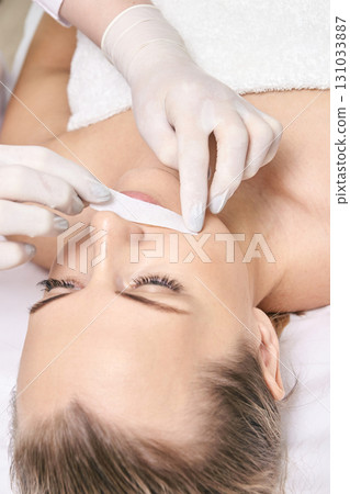 Caucasian female adult undergoing lip hair removal with wax strip by beautician Caucasian female adult undergoing lip hair removal with wax strip by beautician 131033887