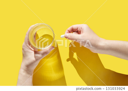 Caucasian female hands holding water glass and medicine pill on vibrant yellow 131033924