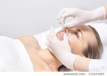 Caucasian female adult receiving cosmetic facial treatment by gloved hands 131033983