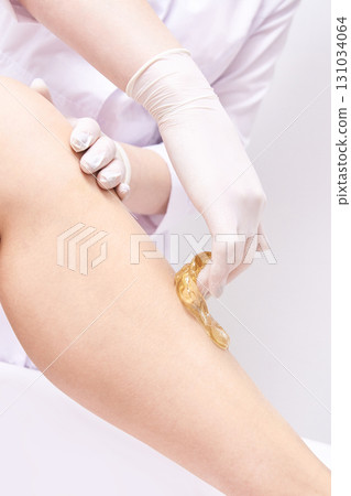 Female leg sugaring hair removal technique with gloved hands in beauty salon Female leg sugaring hair removal technique with gloved hands in beauty salon 131034064