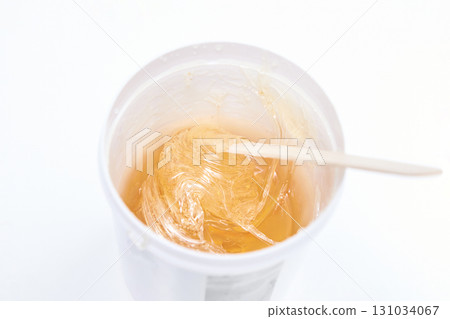 Container of yellow sugar wax with wooden spatula on white background for hair 131034067