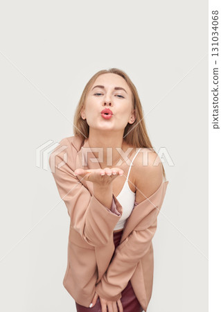 Young caucasian female blowing kiss in stylish beige blazer on light background Young caucasian female blowing kiss in stylish beige blazer on light background 131034068