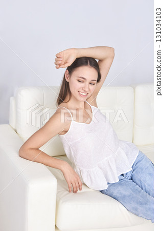 Smiling young caucasian female relaxing on white sofa in casual outfit 131034103