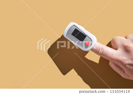 Adult hand using fingertip pulse oximeter on finger against plain background 131034119
