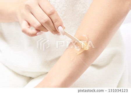 Female caucasian adult applying wax on arm for hair removal using wooden 131034123