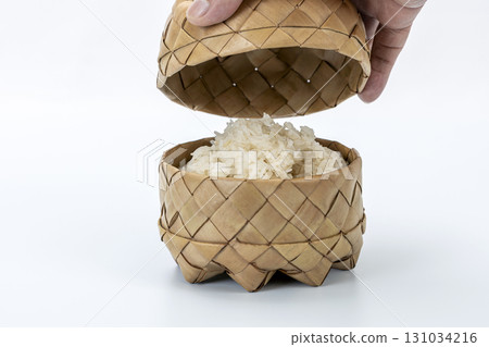 Hand opening woven palm leaf container revealing sticky rice, traditional Asian food presentation, natural material Hand opening woven palm leaf container revealing sticky rice, traditional Asian food presentation, natural material 131034216