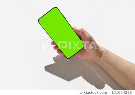 Caucasian adult hand holding smartphone with green screen in bright light Caucasian adult hand holding smartphone with green screen in bright light 131034256