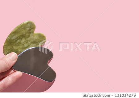 Gua sha tools: green jade and stainless steel massage stone set on soft pink 131034279