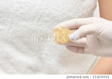 Female caucasian adult hand holding wax product with a white towel background 131034333