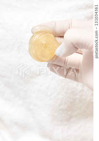 Gloved hand holding honey-colored slime ball on white background Gloved hand holding honey-colored slime ball on white background 131034361