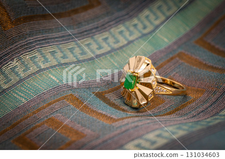 A green emerald ring sits on a blue and brown fabric A green emerald ring sits on a blue and brown fabric 131034603