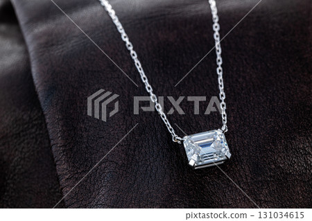 A necklace with a large diamond pendant is displayed on a dark surface 131034615