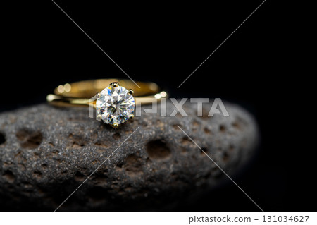 A gold and diamond ring is sitting on a rock 131034627