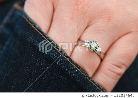 A person is wearing a green ring with a diamond and a sapphire 131034645