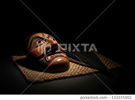 Traditional wooden indonesian topeng demon mask with a hand fan on a dramatic black background 131035002