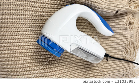 A lint remover against a warm cozy sweater with bobbles. Preparing wardrobe and caring for clothes, clothing care and maintenance, fall and winter fashion and garment preparation 131035995