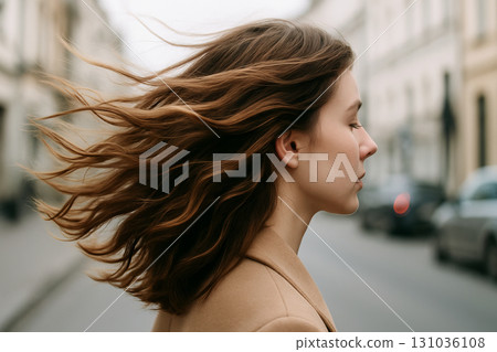 Woman with flowing hair walking in urban street captured in profile view. concept of urban lifestyle, windy day, fashion confidence 131036108