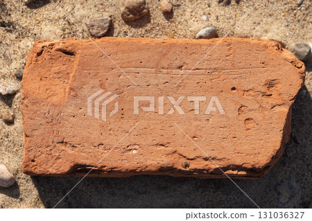 A solitary brick lying on sandy soil, highlighting its texture and earthy color 131036327