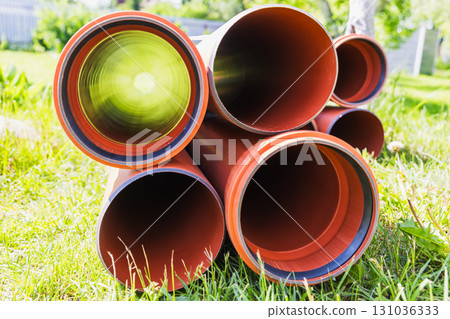An arrangement of new bright orange piping stacked on a patch of lush green grass 131036333