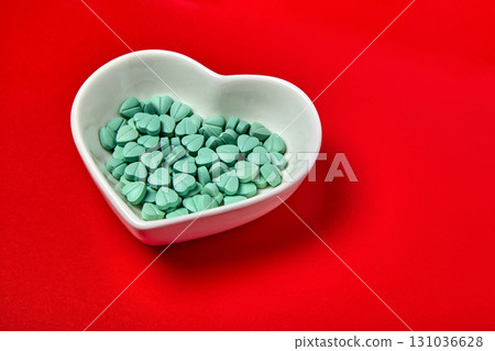 turquoise colored cardiology pills in white ceramic heart shaped bowl on red background 131036628