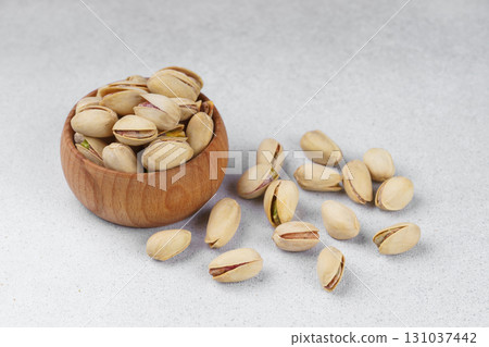 Little wooden bowl with salted pistachio nuts and scattered seeds on gray background close up 131037442