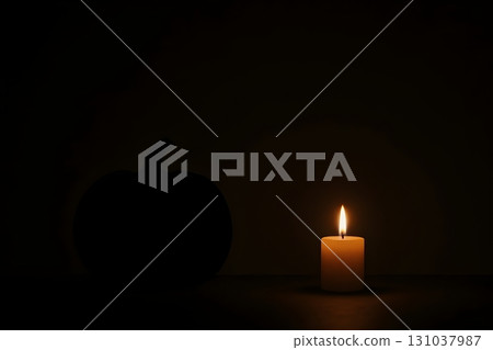 Single candle burning in darkness beside a pumpkin silhouette, warm glow creating a moody 131037987