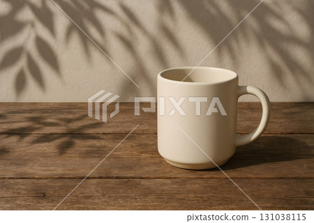 Cream ceramic mug on rustic wooden table with soft leaf shadows on the wall Cream ceramic mug on rustic wooden table with soft leaf shadows on the wall 131038115